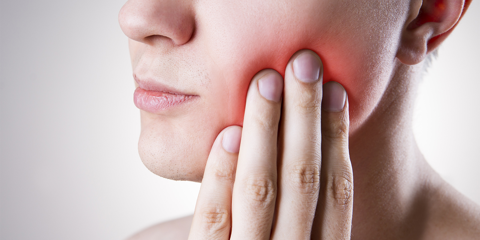 歯が痛み、頬を手でおさえる男性