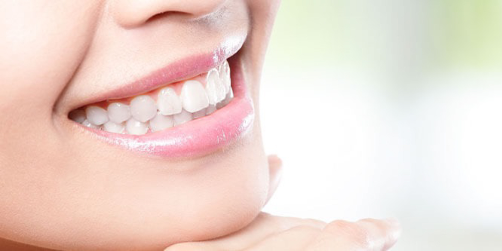 顎を手に置き、白い歯を見せながら微笑む女性の口元