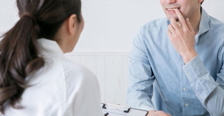 自身の歯を指さし見せる男性と、それを確認し記録する女性スタッフ