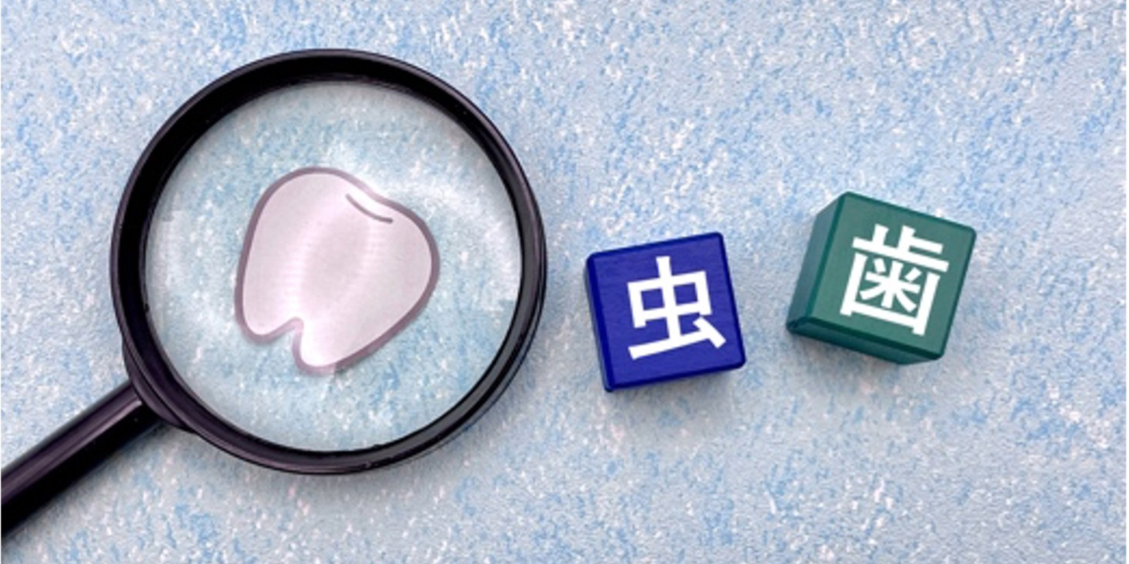 虫眼鏡の先に歯のイラスト、横に虫歯の文字