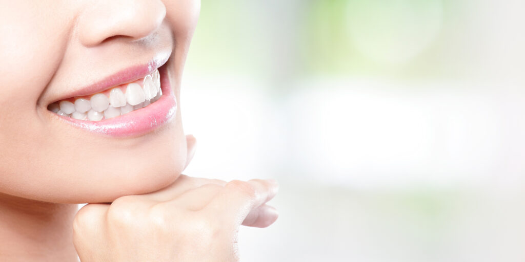 顎を手に置き、白い歯を見せながら微笑む女性の口元