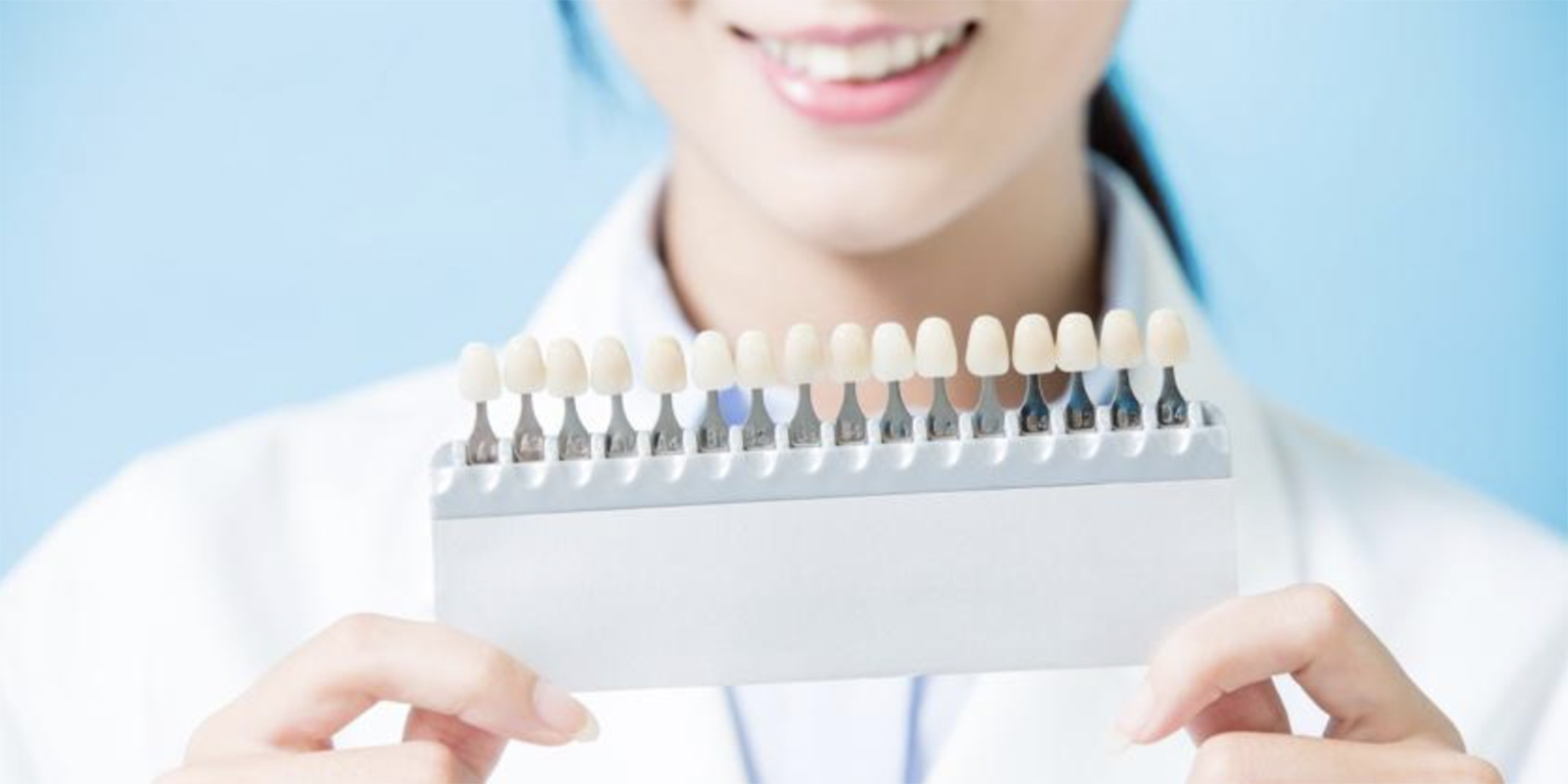 シェードガイドという色を確認するための歯の見本を持ち微笑む女性