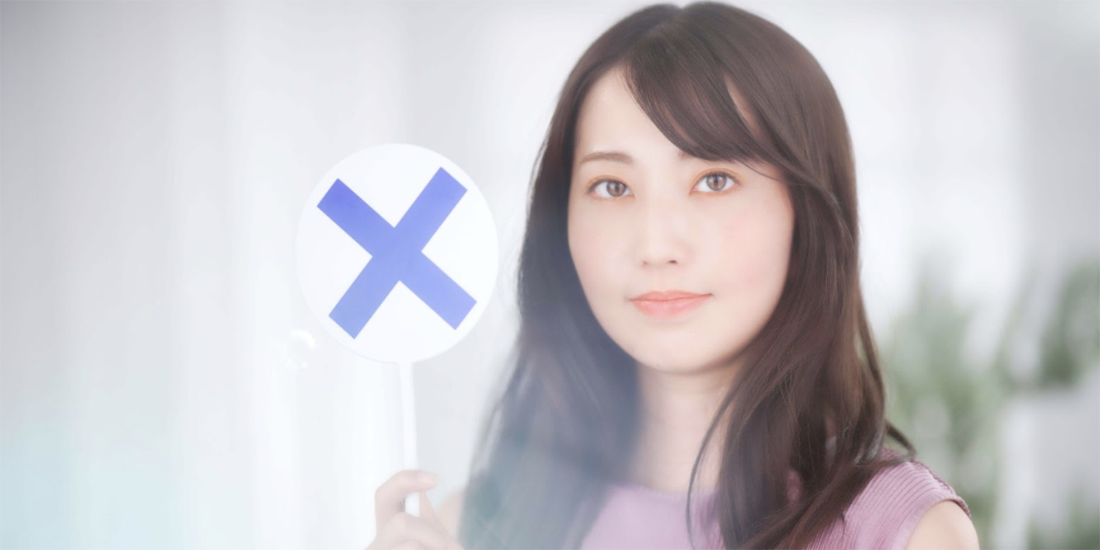 バツの書かれた札を見せる女性